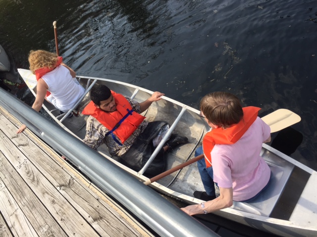 Three people in a canoe, one student in the middle, and two teachers. They are about to get out of the canoe onto the dock.