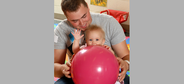 Young dad and baby girl playing with a big red ball