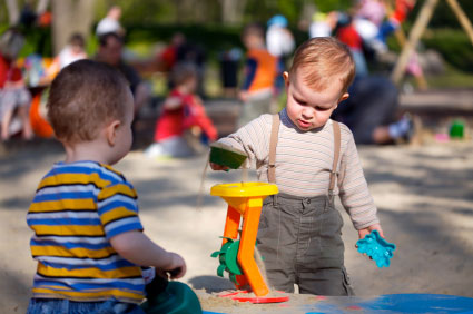 Two toddlers playing in a sandbox together