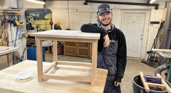 Student showing off wooden table that he built